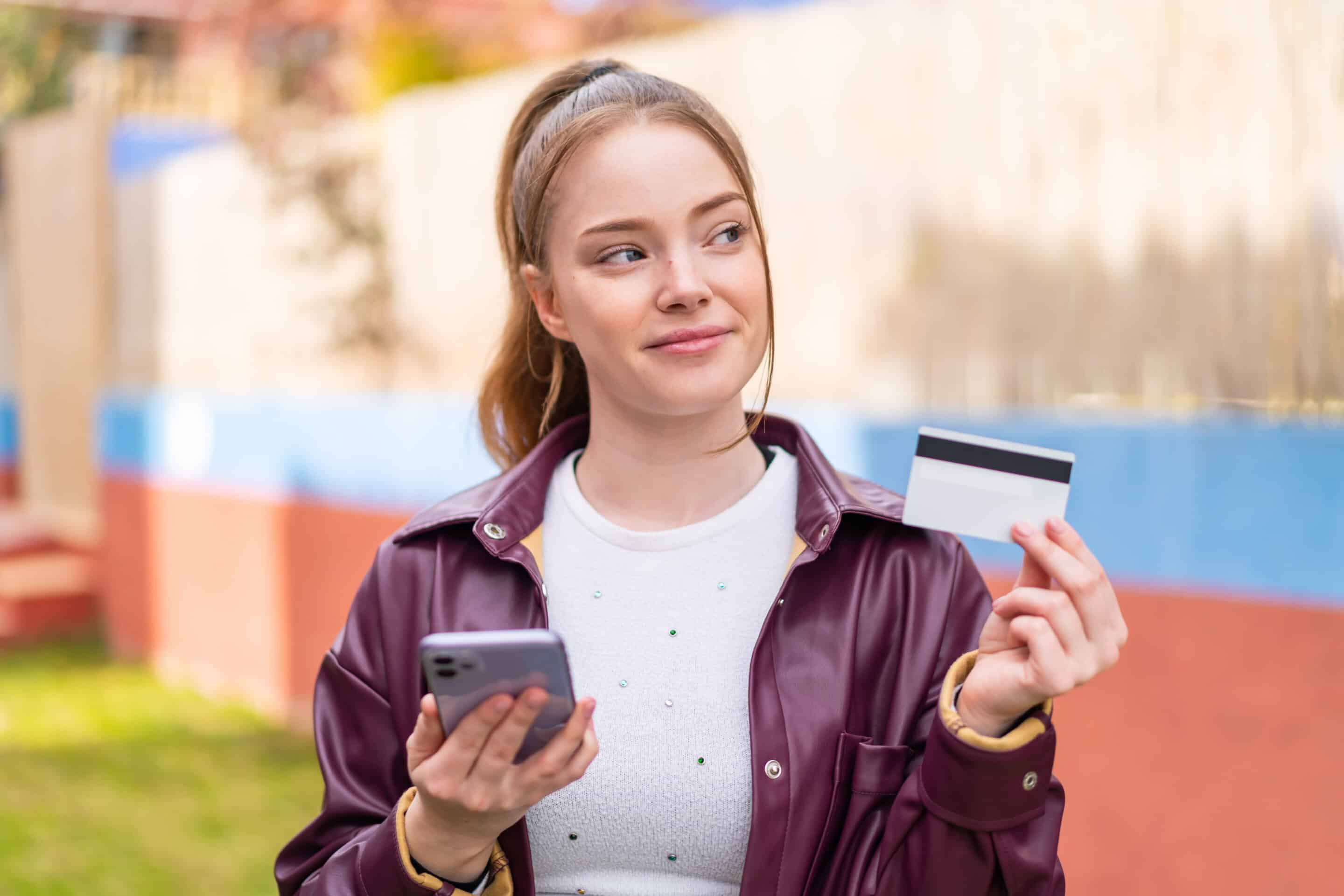 Sachbezugskarte - Junge Frau freut sich über Ihre Sachbezugskarte und hat Ihr Handy in der Hand