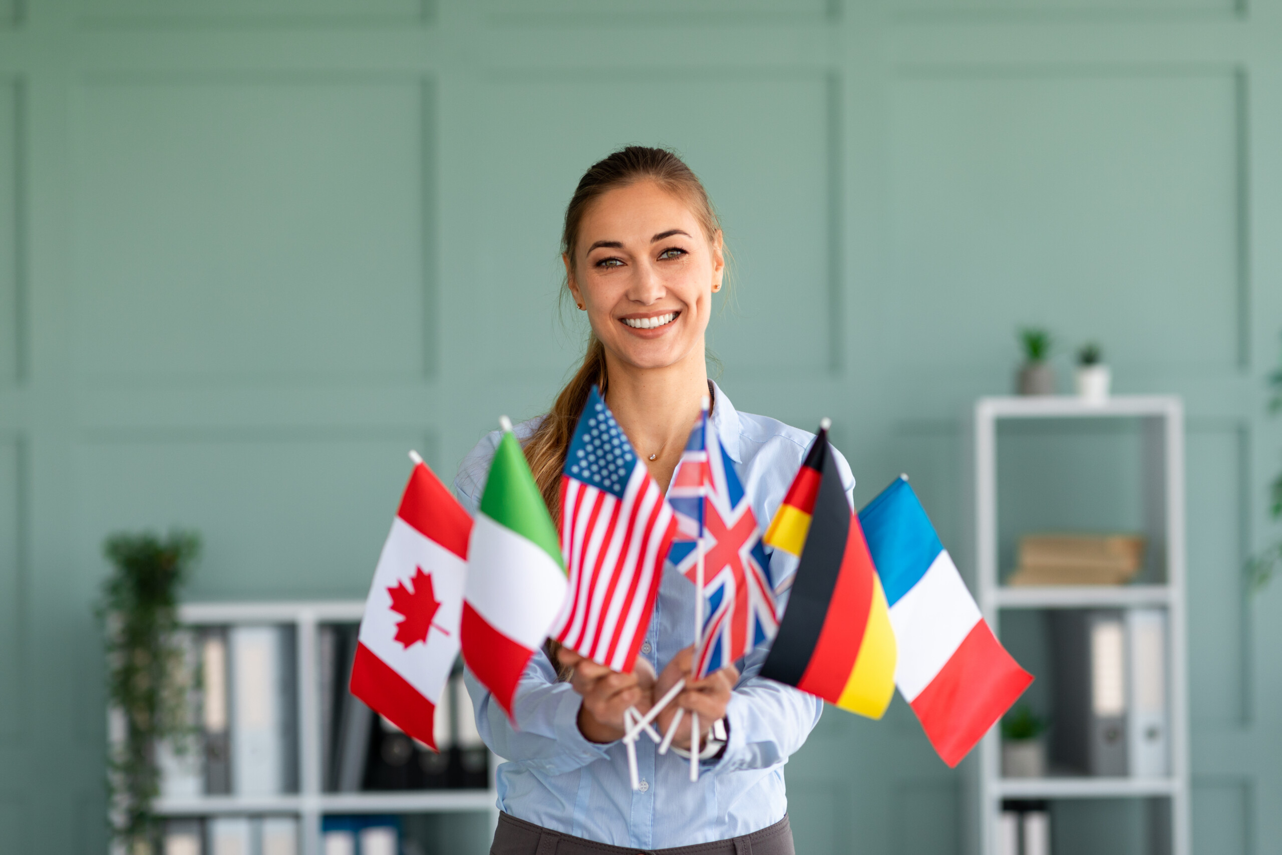 Happy female tutor showing bunch of diverse flags, recommending foreign language studying school Händeschütteln nach Mitarbeiter präsentieren mit Mock-up-Kreditkarte Zahlungen an Geschäftskunden. Bereit, Rabatte und Lebensversicherungen anzubieten.